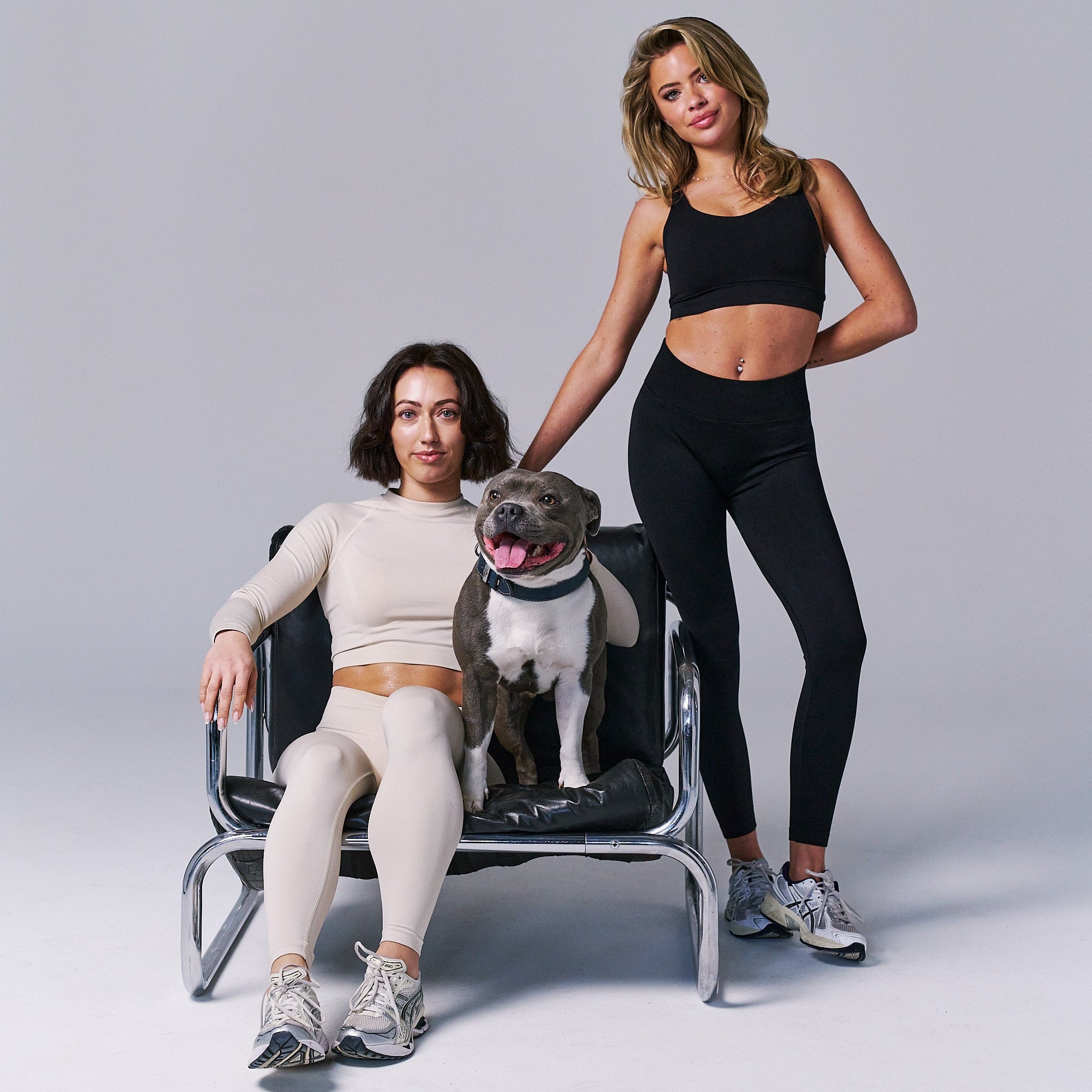 Two women and a dog sitting on a chair against a gray background